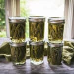 6 cans of dilly beans stacked in 2's on a counter with a window in the background.