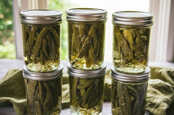 6 cans of dilly beans stacked in 2's on a counter with a window in the background.