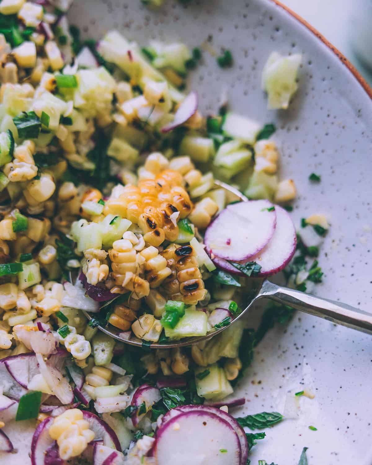 Close up of finished summer corn salad in a bowl with a serving spoon.