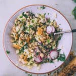 Grilled corn salad with radish and cucumber and fresh herbs, in a white bowl with a red rim, top view.