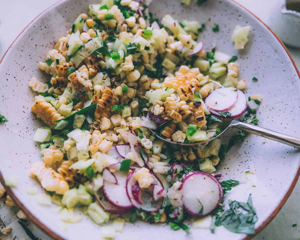 Grilled corn salad in a bowl with a spoon digging into it to serve. 