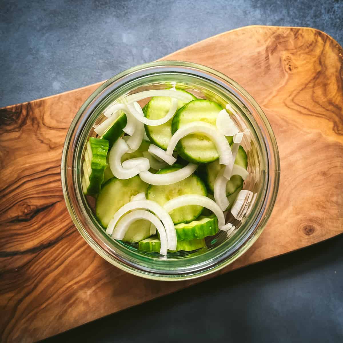Top view of quart jar with layers of cucumber and onions, on a wood cutting board. 