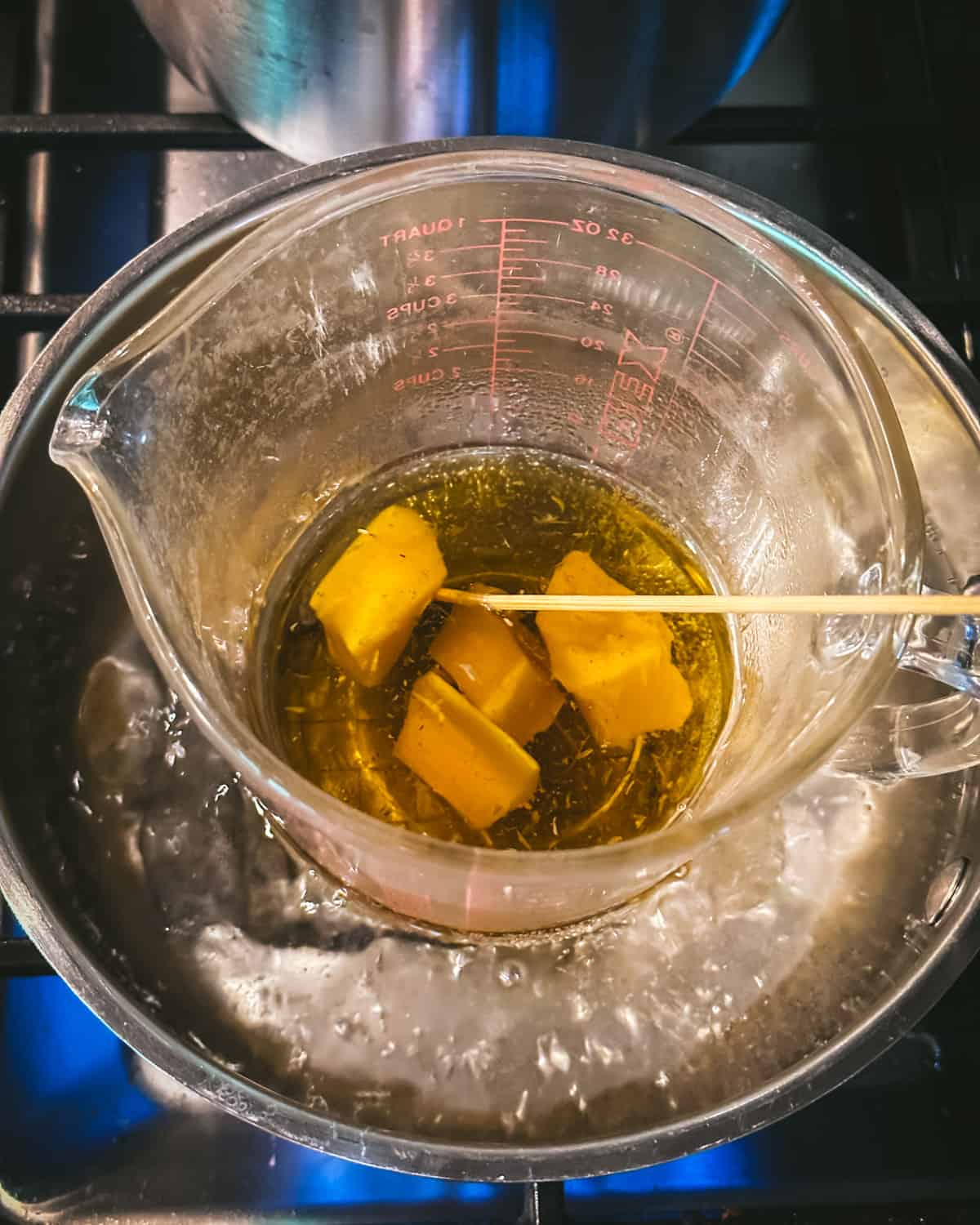 A make shift double boiler with melting beeswax and a bamboo skewer stirring it. 