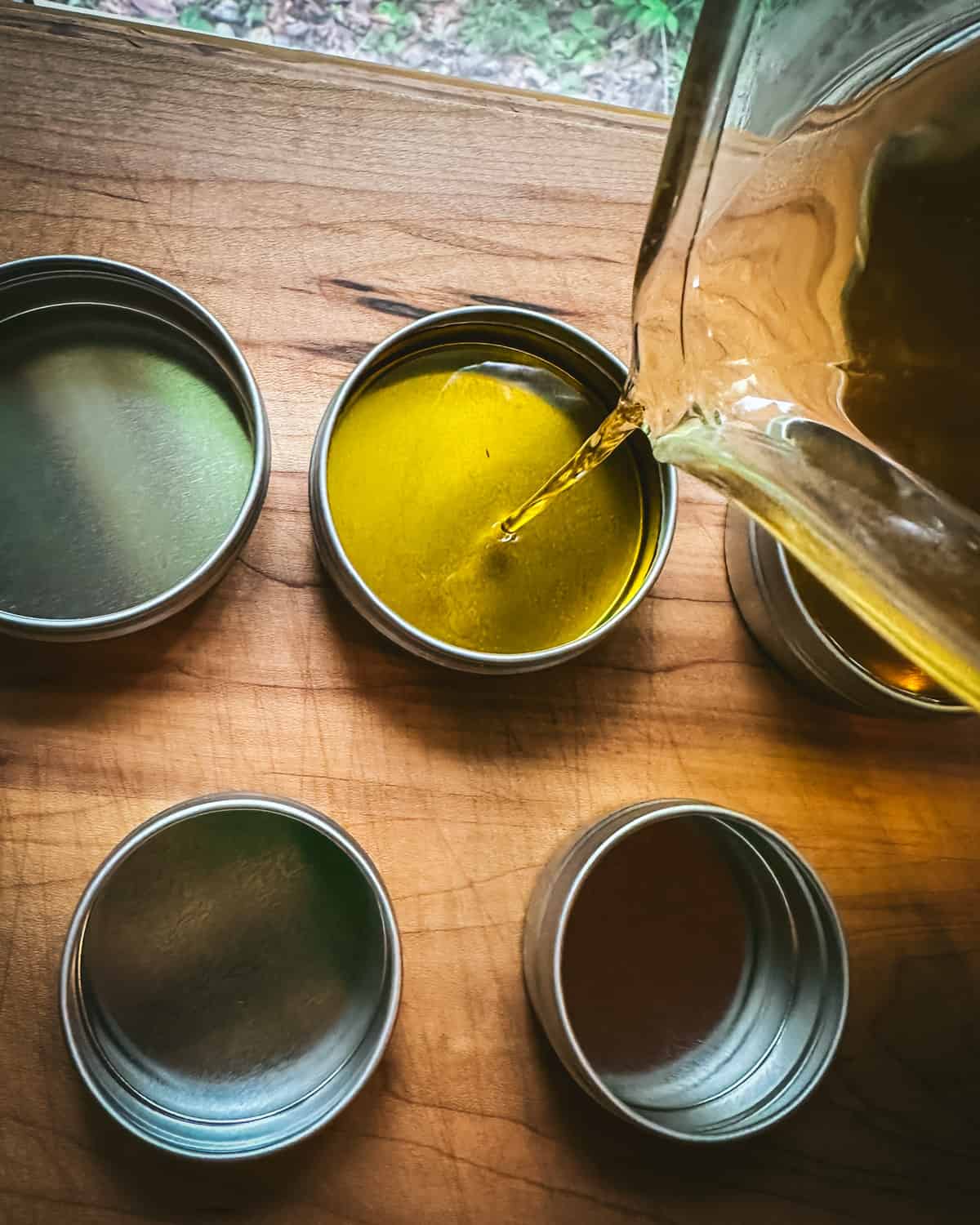 Warm yarrow salve pouring into tins sitting on a wood surface. Top view. 