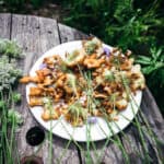 A plate of fried Queen Anne's lace flowers on a white plate, outside on a wood table with fresh Queen Anne's Lace flowers surrounding.