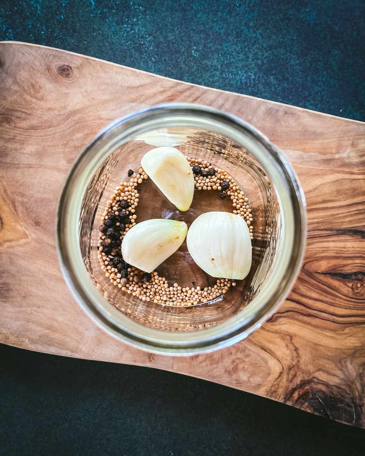A jar with garlic cloves and pickling spices on a wood cutting board. Top view. 