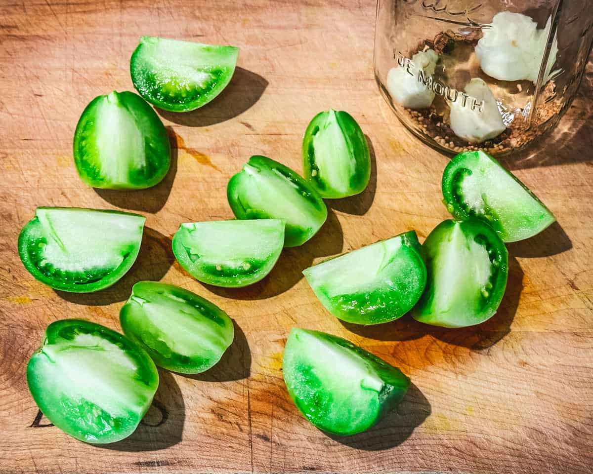 Green tomatoes cut into wedges on a wood cutting board. 
