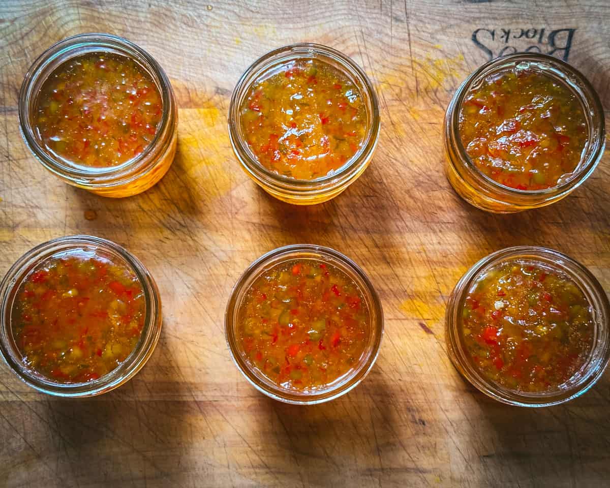 Jars filled with pepper jelly on a wooden cutting board, top view. 