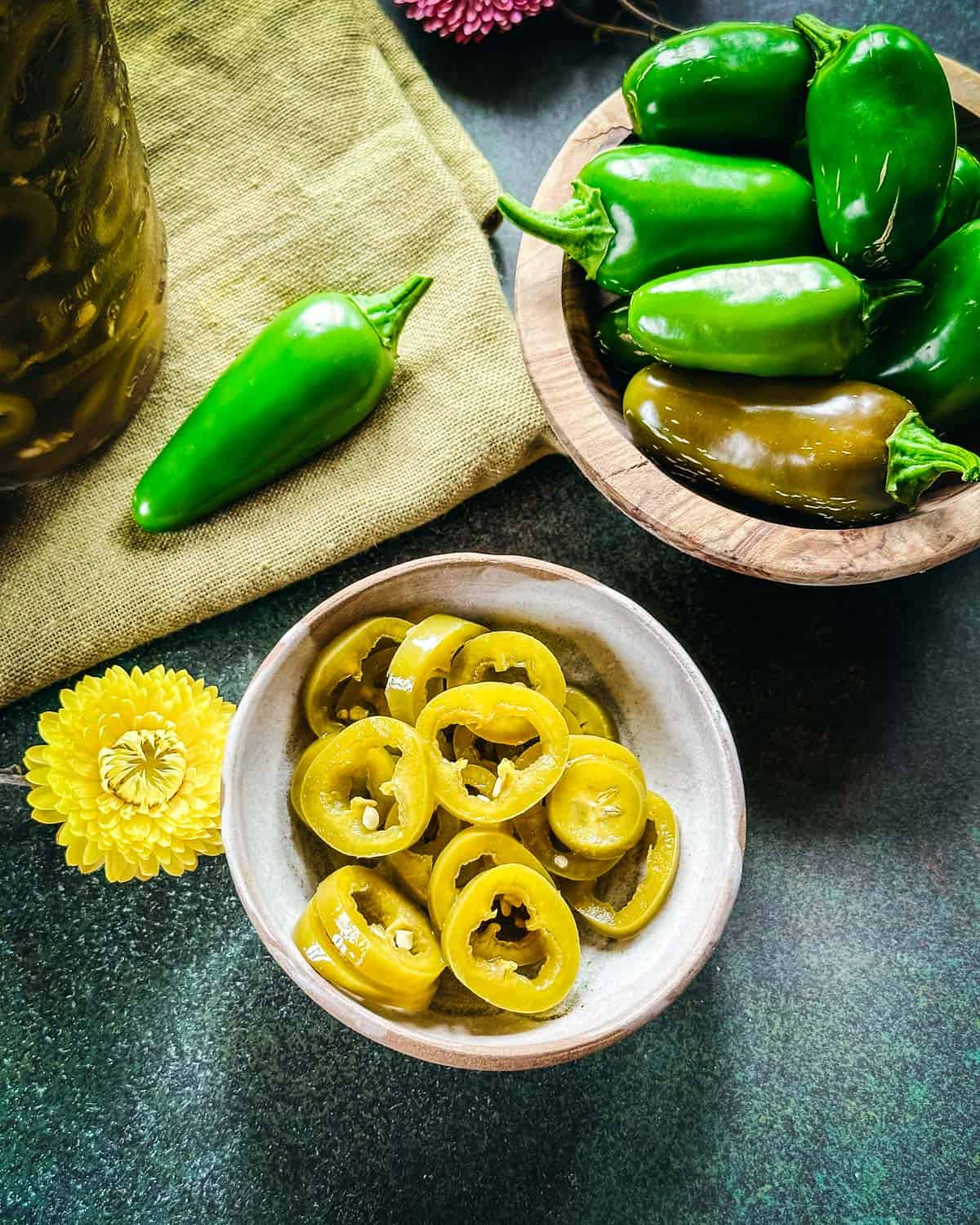 A bowl of pickled jalapeños nest to a bowl of fresh jalapeños, top view. 
