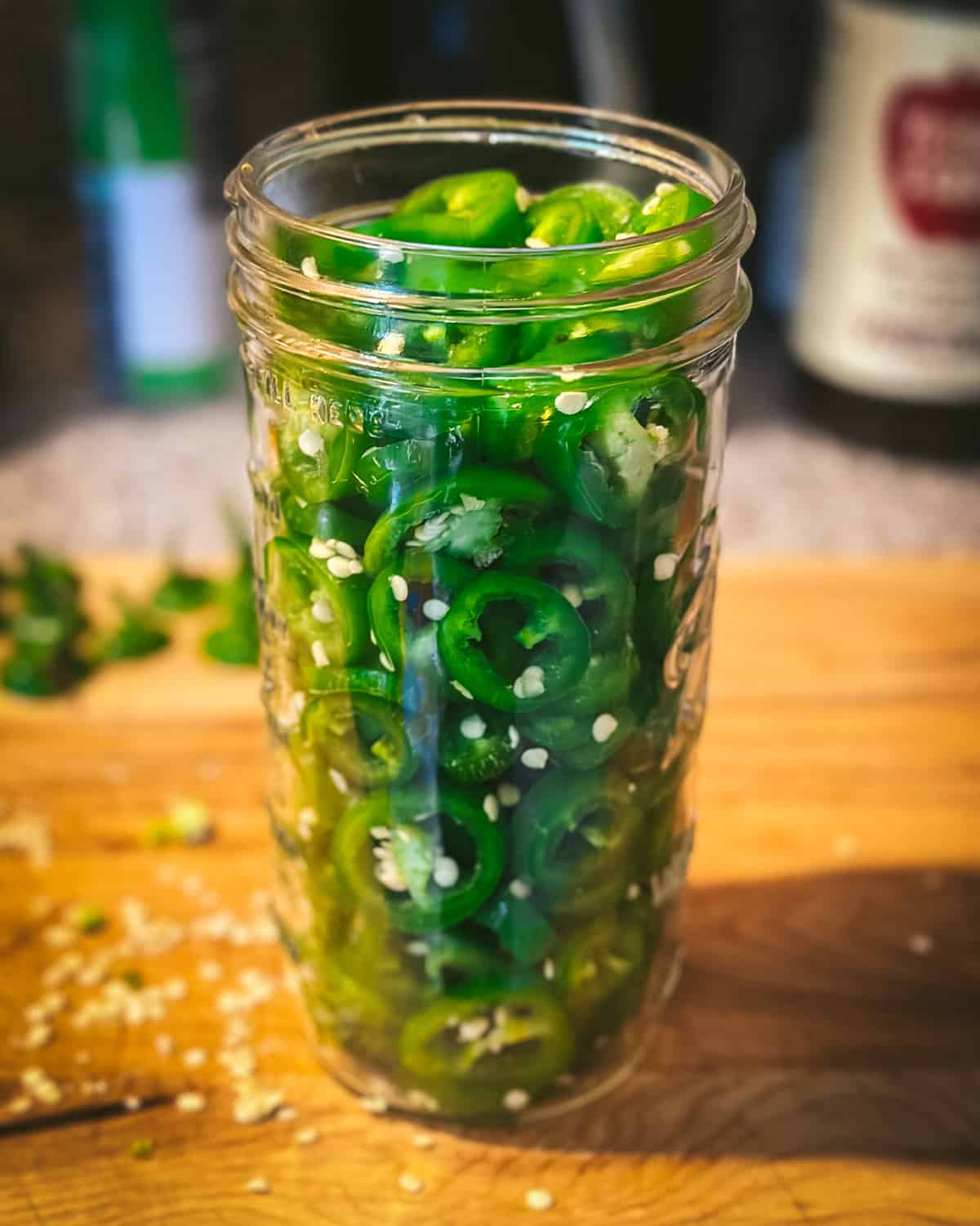 A quart jar filled with sliced jalapeños on a wood cutting board. 