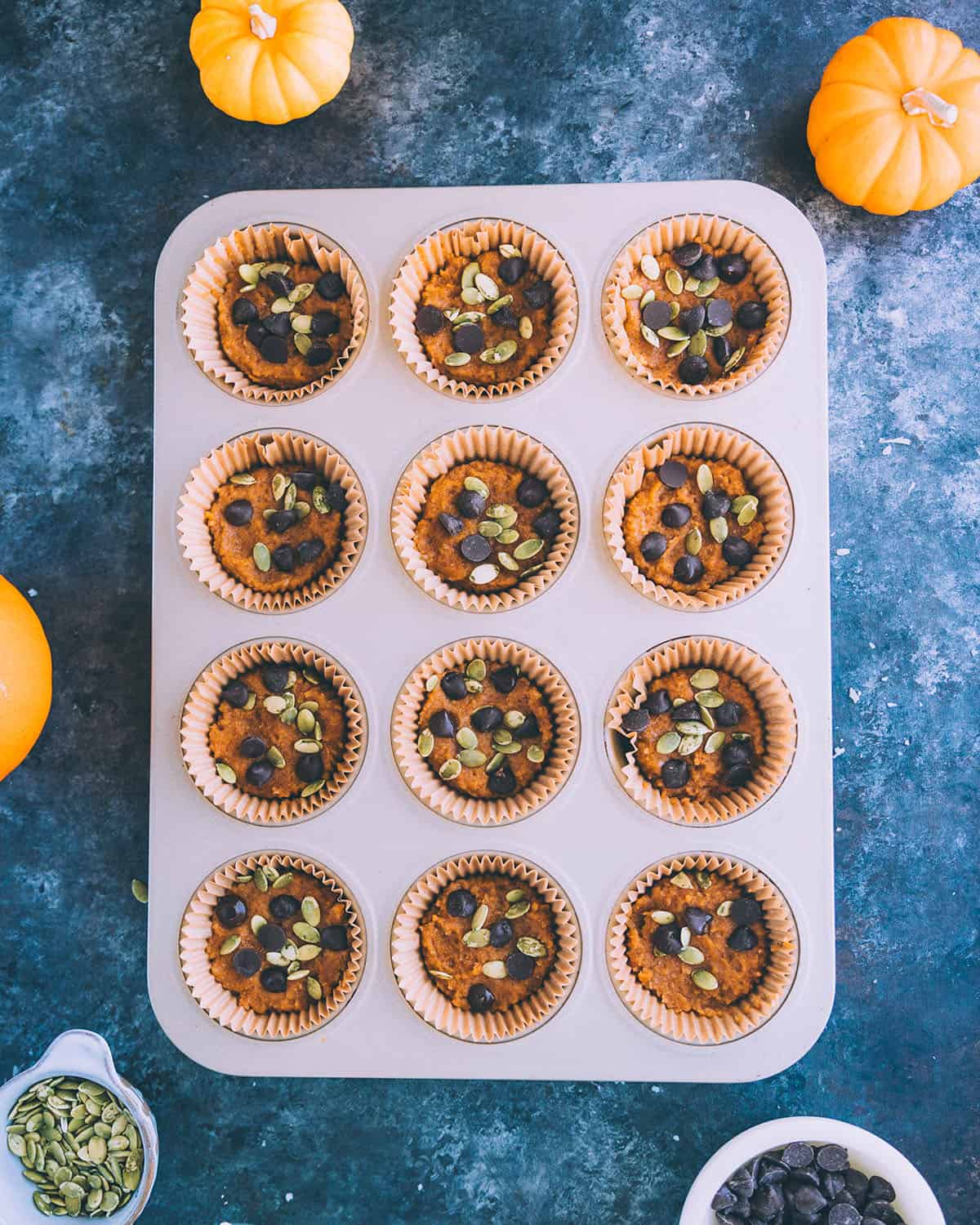 Coconut pumpkin cups with chocolate chips and pumpkin seeds on top in a muffin tin, top view. 