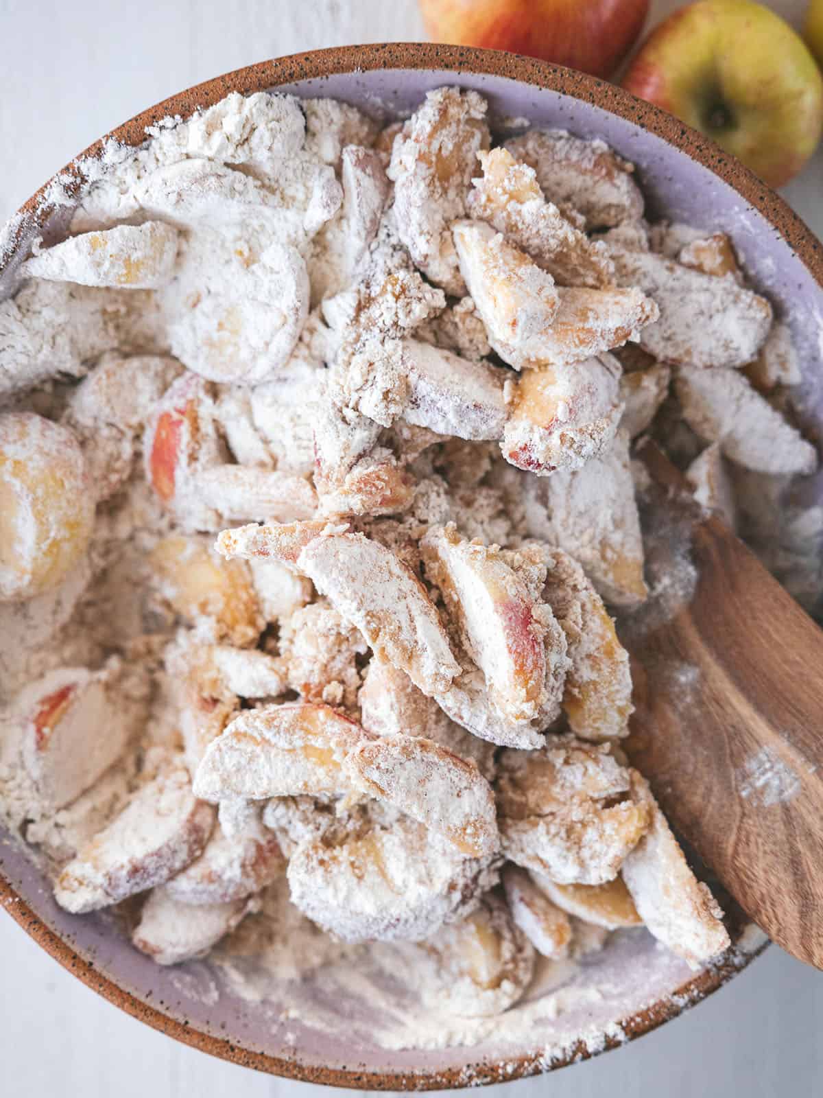 Apple slices mixing with the dry ingredients with a wooden spoon, top view. 