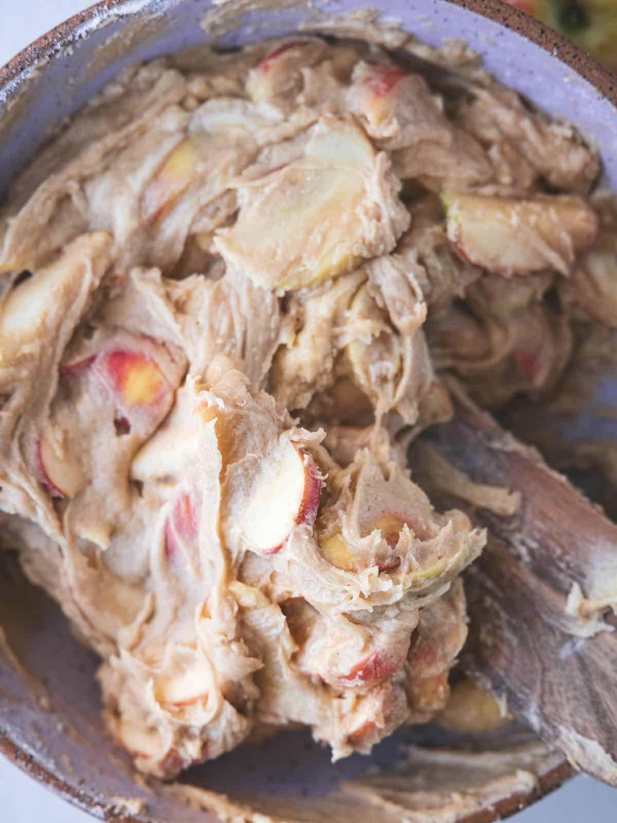 Apples mixed with batter being stirred with a wooden spoon, top view. 