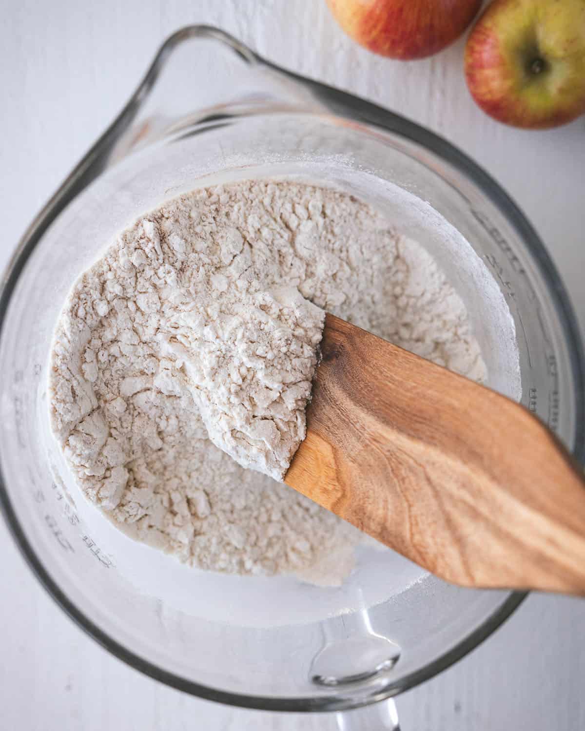 A clear bowl with a wooden spoon stirring the dry ingredients, top view. 