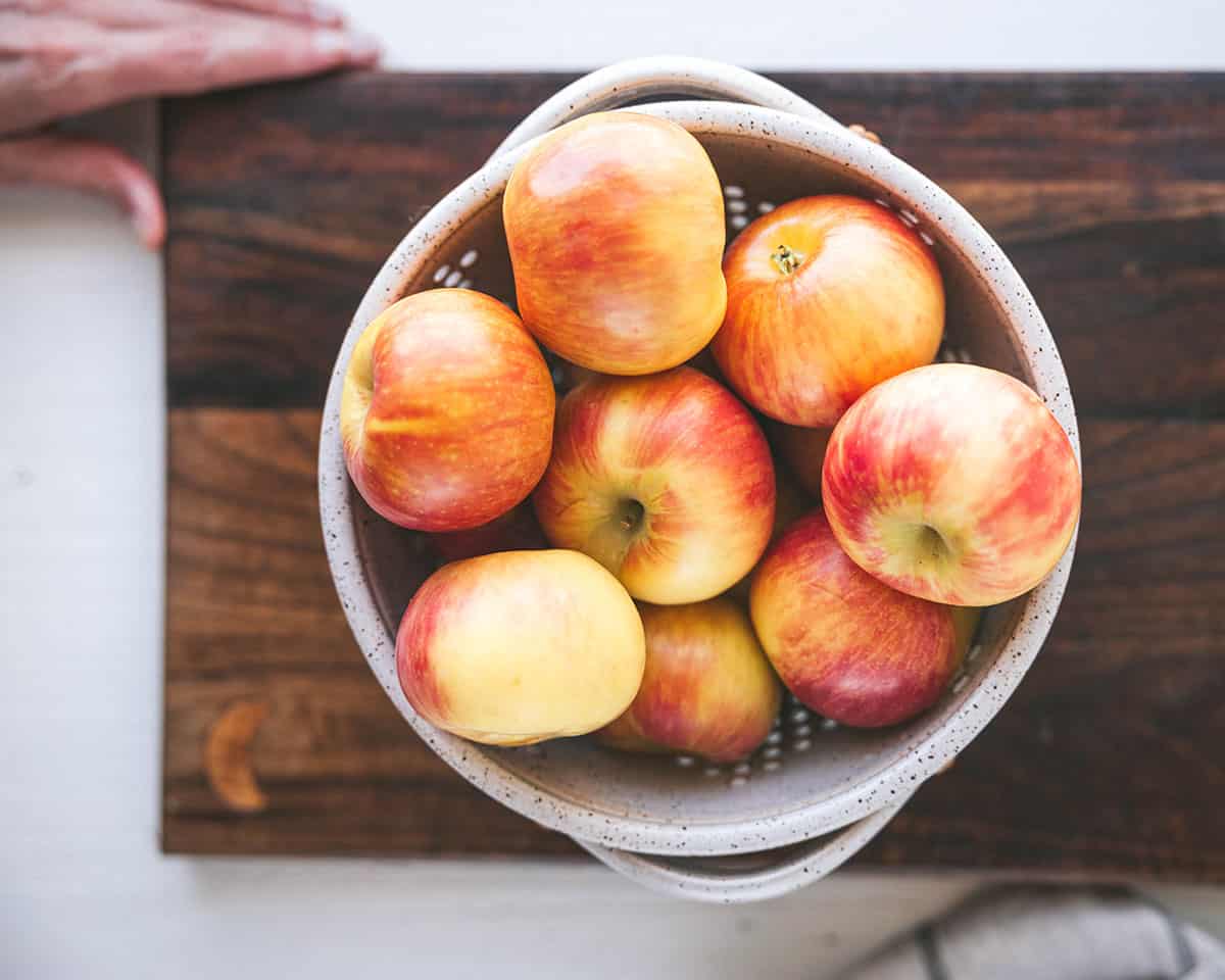 Whole apples in a bowl on a dark wood cutting board. Top view. 