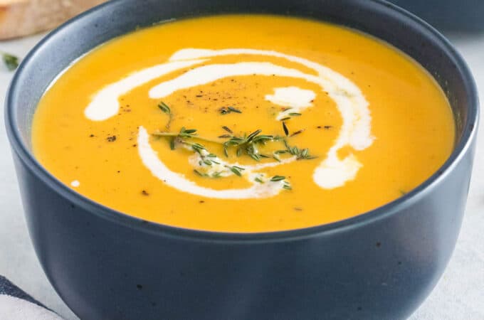 A black bowl with butternut squash soup in it, and a white swirl of cream and spices on top.