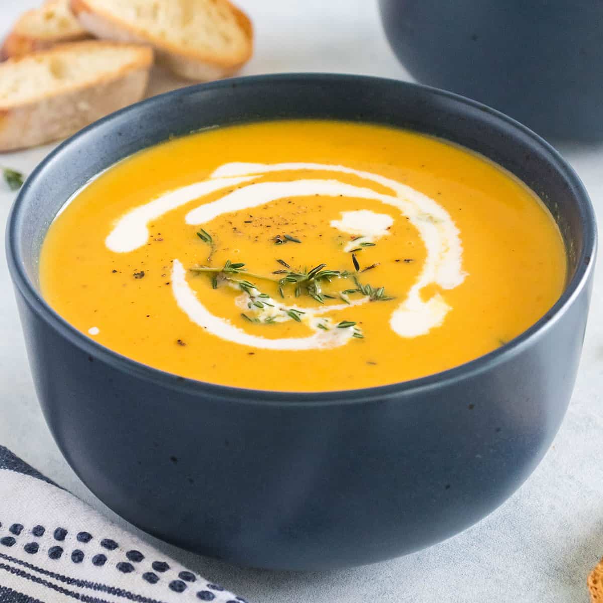 A black bowl with butternut squash soup in it, and a white swirl of cream and spices on top. 