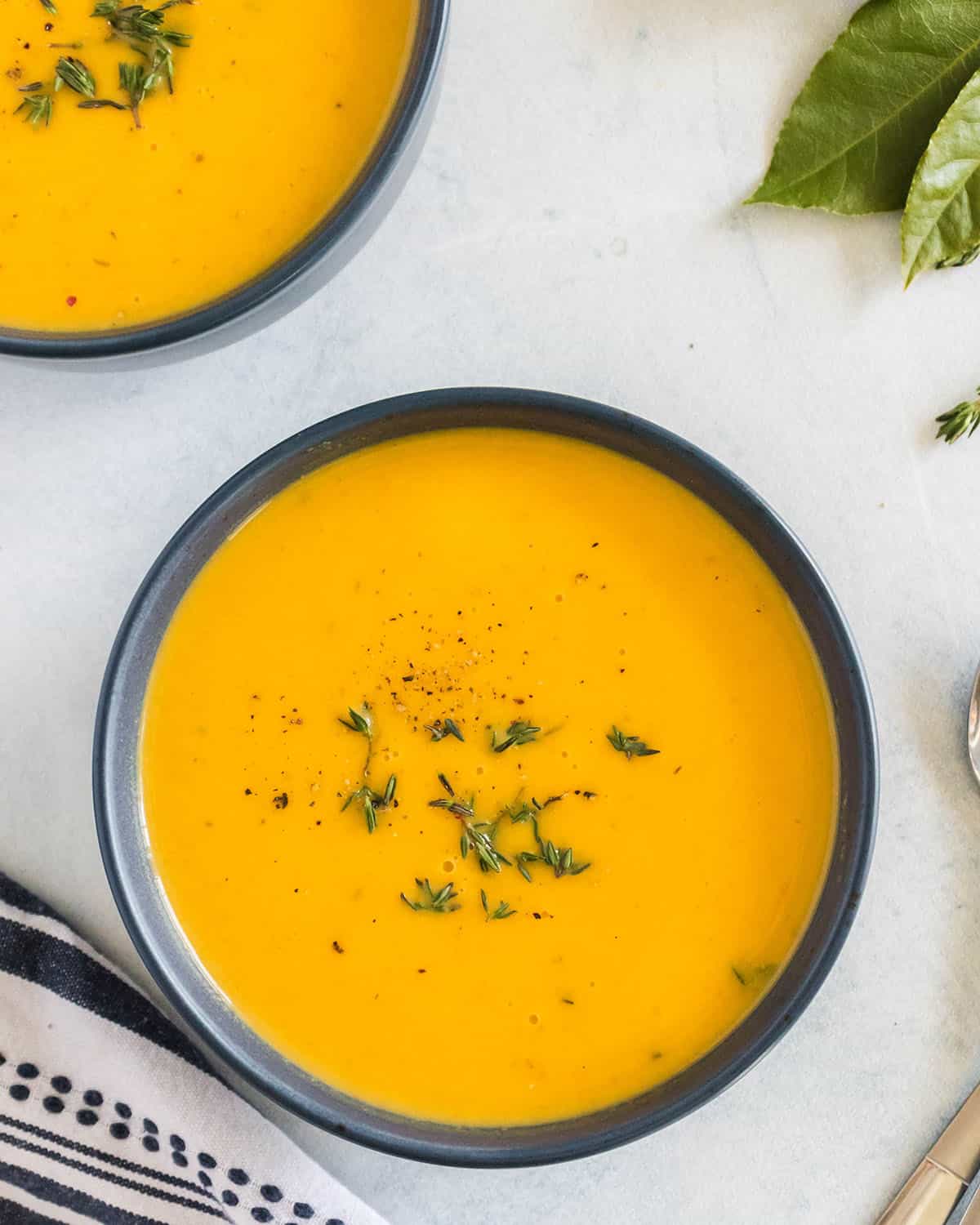 A bowl of butternut squash soup topped with fresh thyme, top view. 
