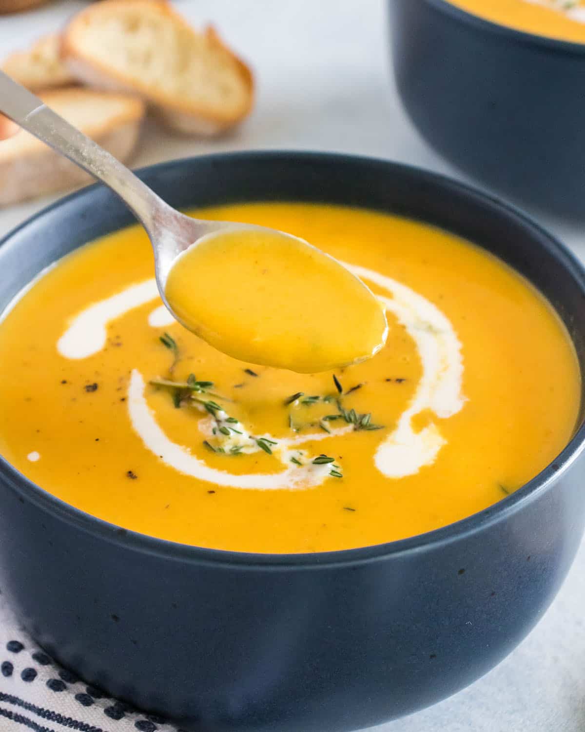 A black bowl of butternut squash bisque topped with a drizzle of heavy cream and spices, with a spoonful lifting out of the bowl 