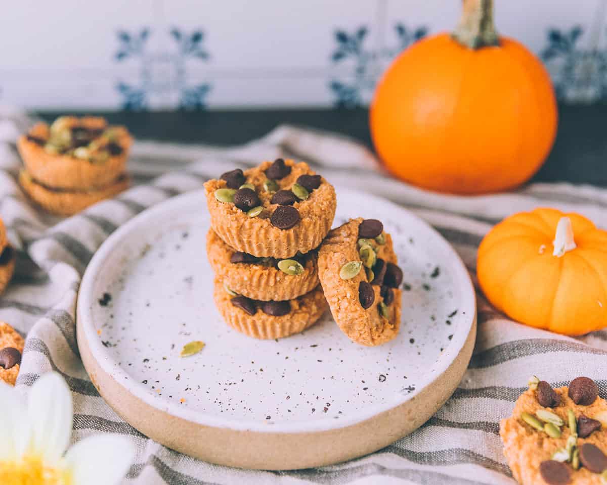 A stack of pumpkin coconut cups on a white plate surrounded by other pumpkin cups and fresh pumpkins. 