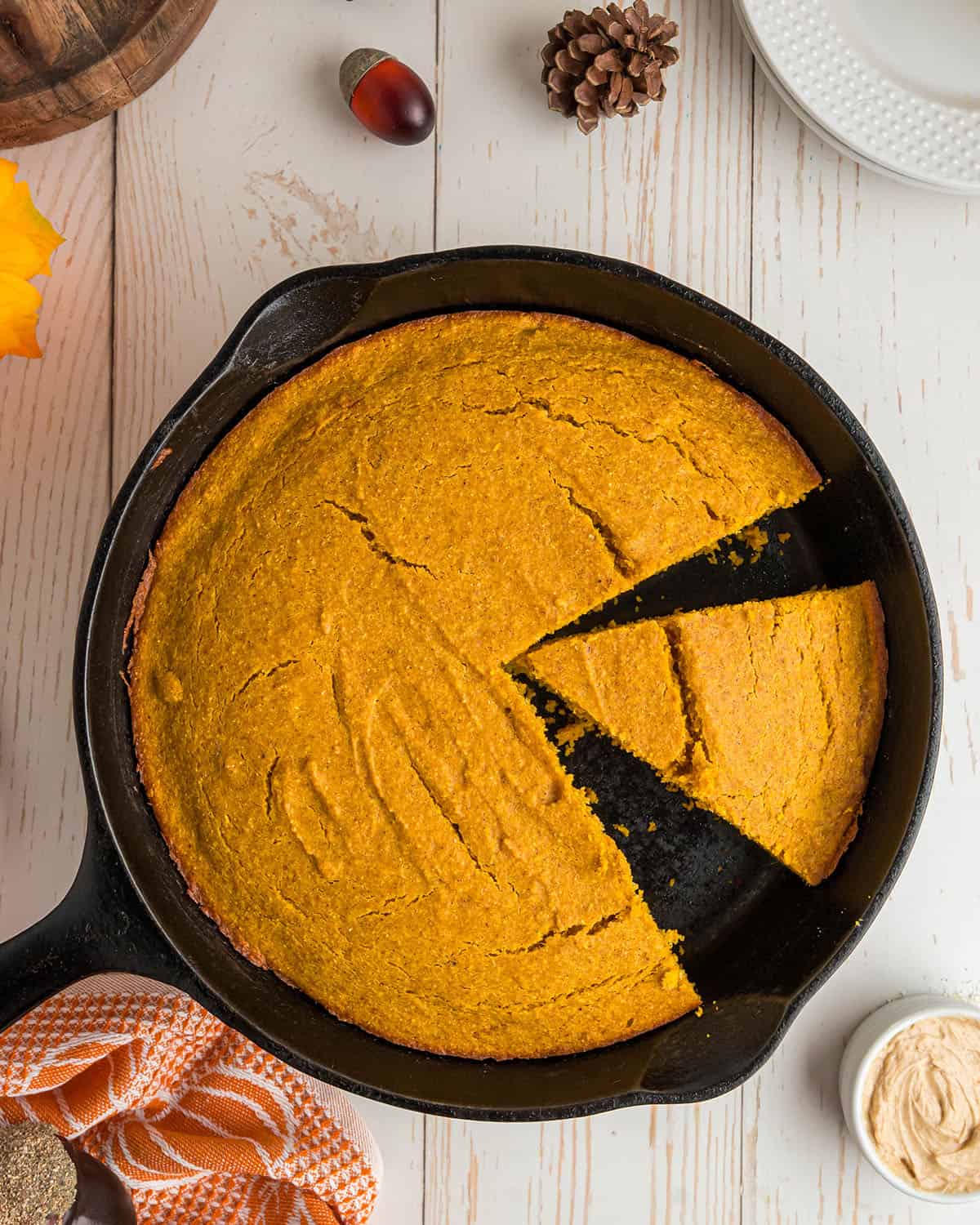 Pumpkin cornbread in a skillet, with a few wedges cut out of it and one ready to serve. Top view. 