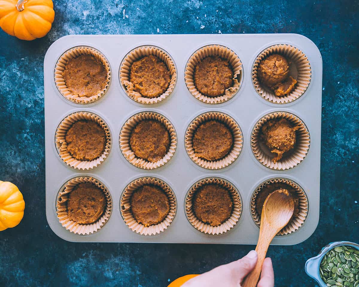 A small wooded spoon pressing the pumpkin coconut mixture down into the tin. 