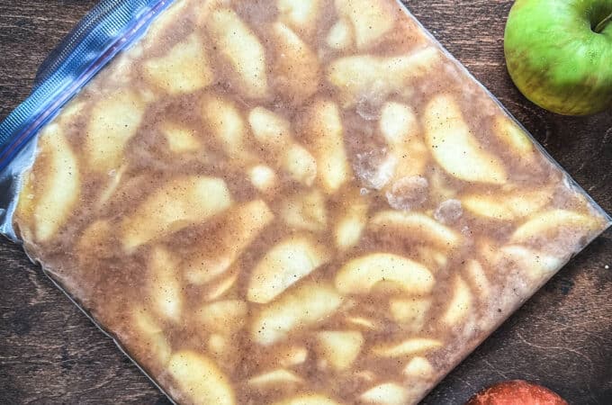 A bag of frozen apple pie filling on a wood surface surrounded by fresh whole apples. Top View.