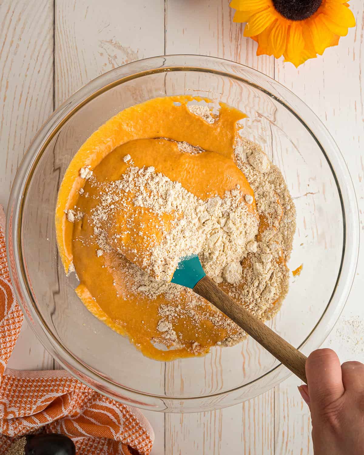 Pumpkin cornbread ingredients being mixed together in a clear bowl, top view. 