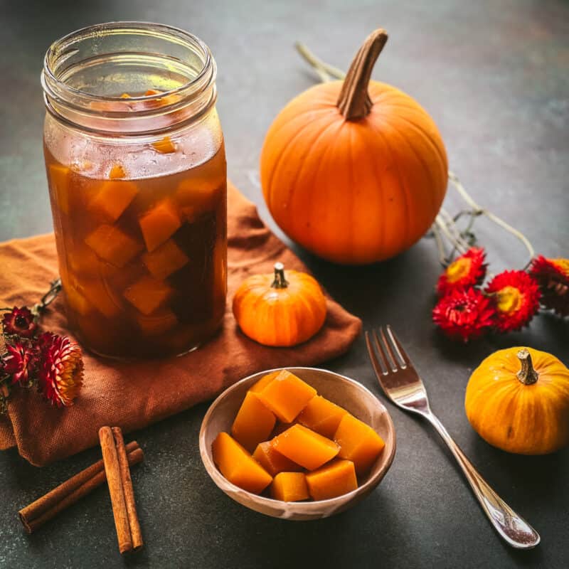 A bowl of pumpkin pickles on a table with a quart jar of pickled pumpkin and small sugar pumpkins