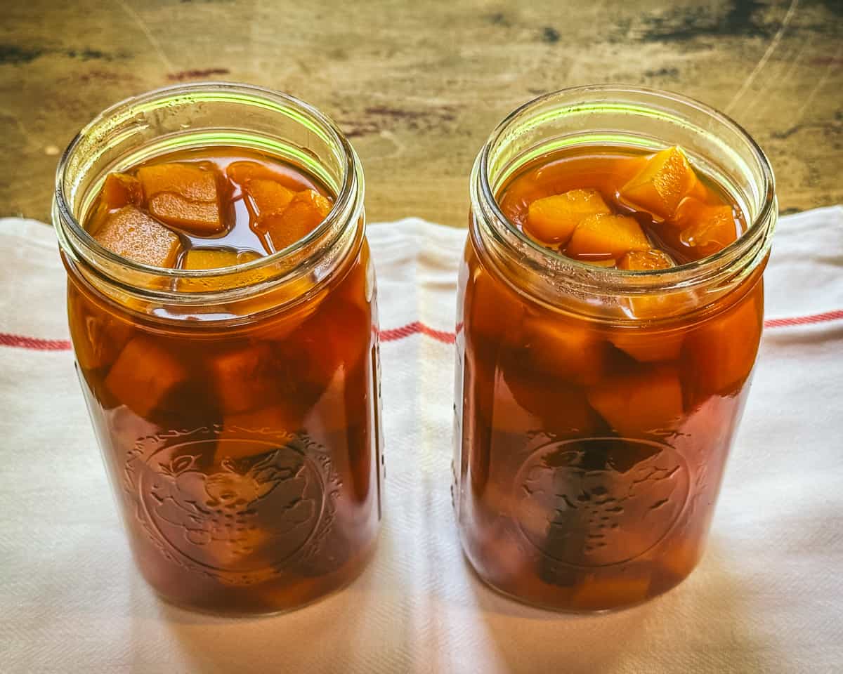 2 jars filled with pumpkin cubes and vinegar brine, each with a cinnamon stick. 