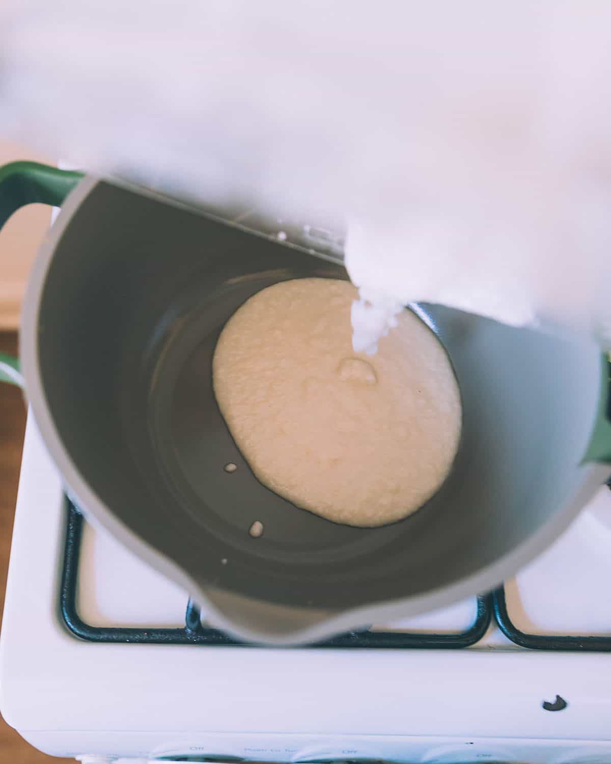 Coconut butter being poured into a small pot on a white stove, top view. 