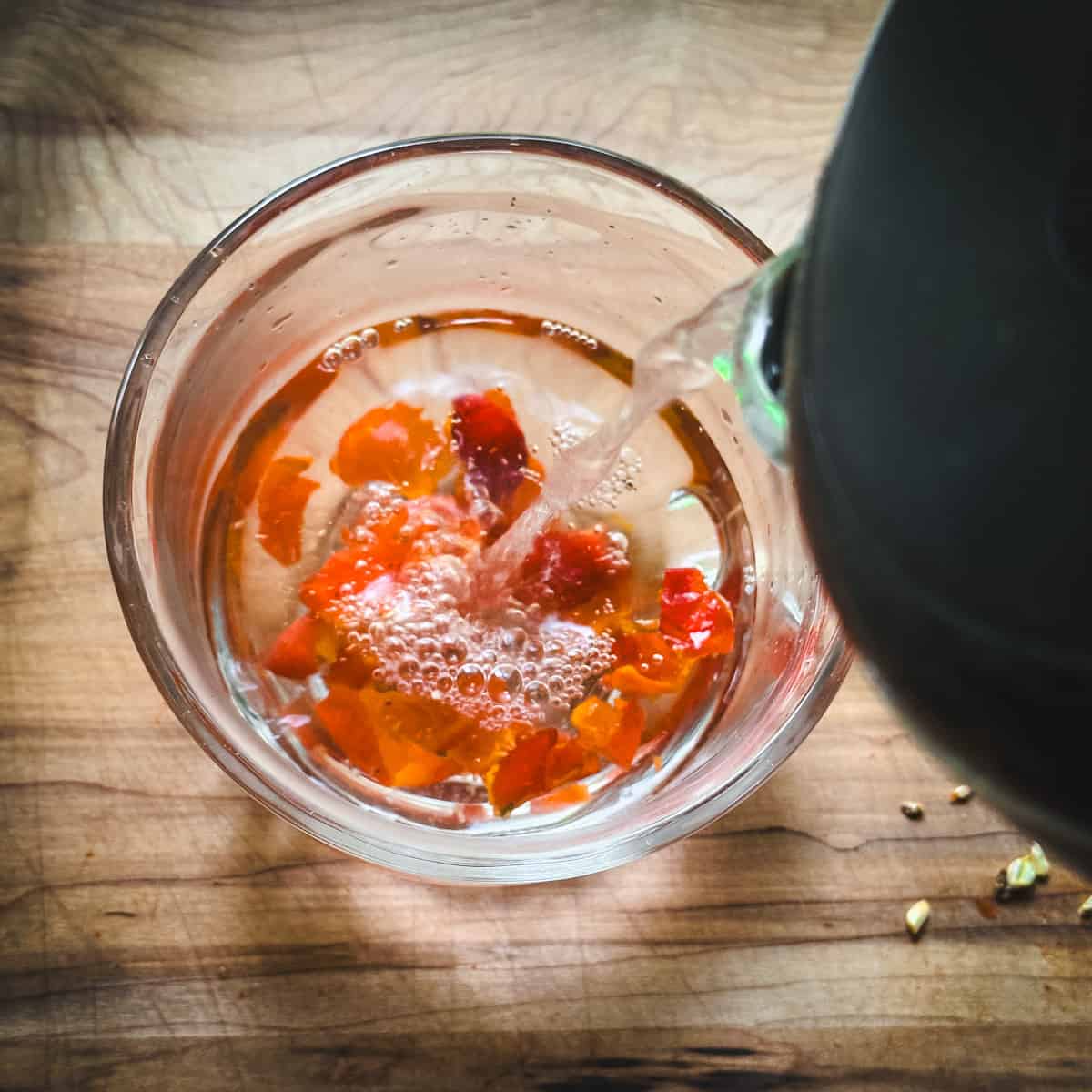 A clear mug with rose hips at the bottom, with hot water pouring over them from a kettle, top view. 