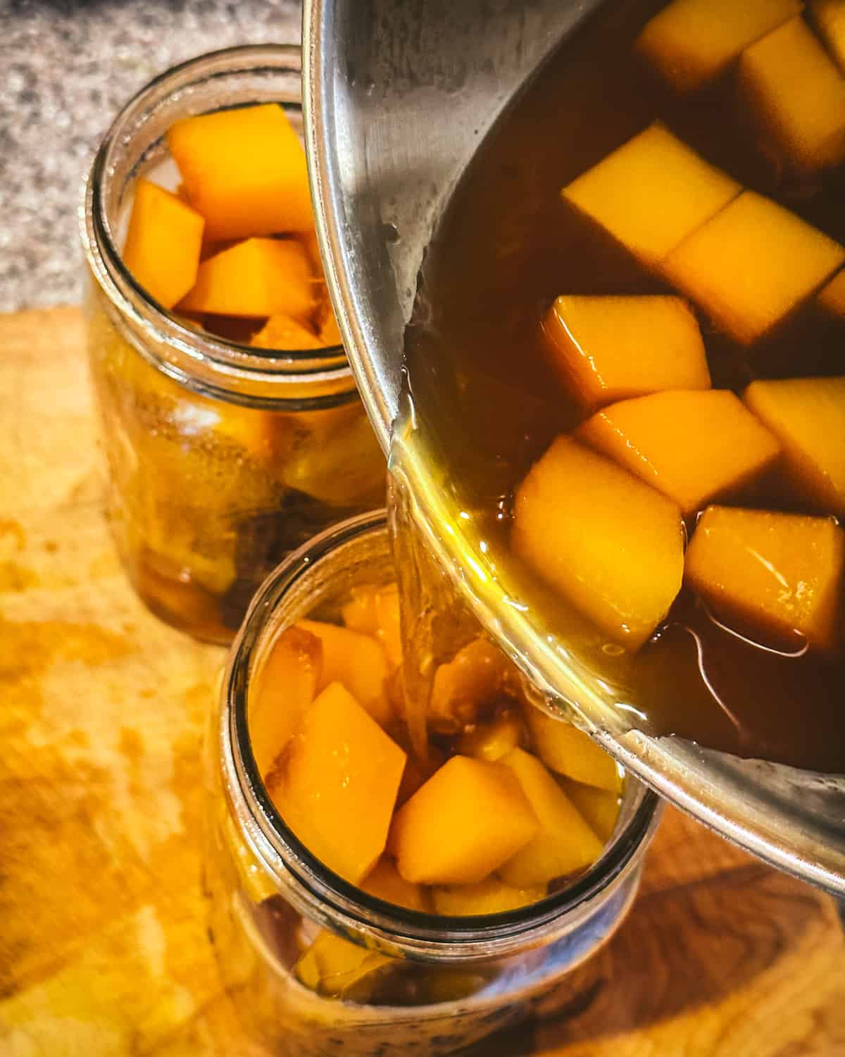 Pumpkin cubes and vinegar brine pouring from a pot into two jars. 