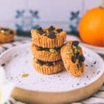 A stack of pumpkin coconut butter cups on a white plate with a pumpkin in the background.