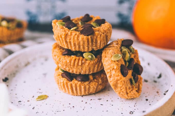 A stack of pumpkin coconut butter cups on a white plate with a pumpkin in the background.