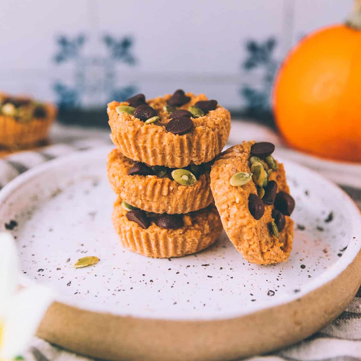 A stack of pumpkin coconut butter cups on a white plate with a pumpkin in the background. 