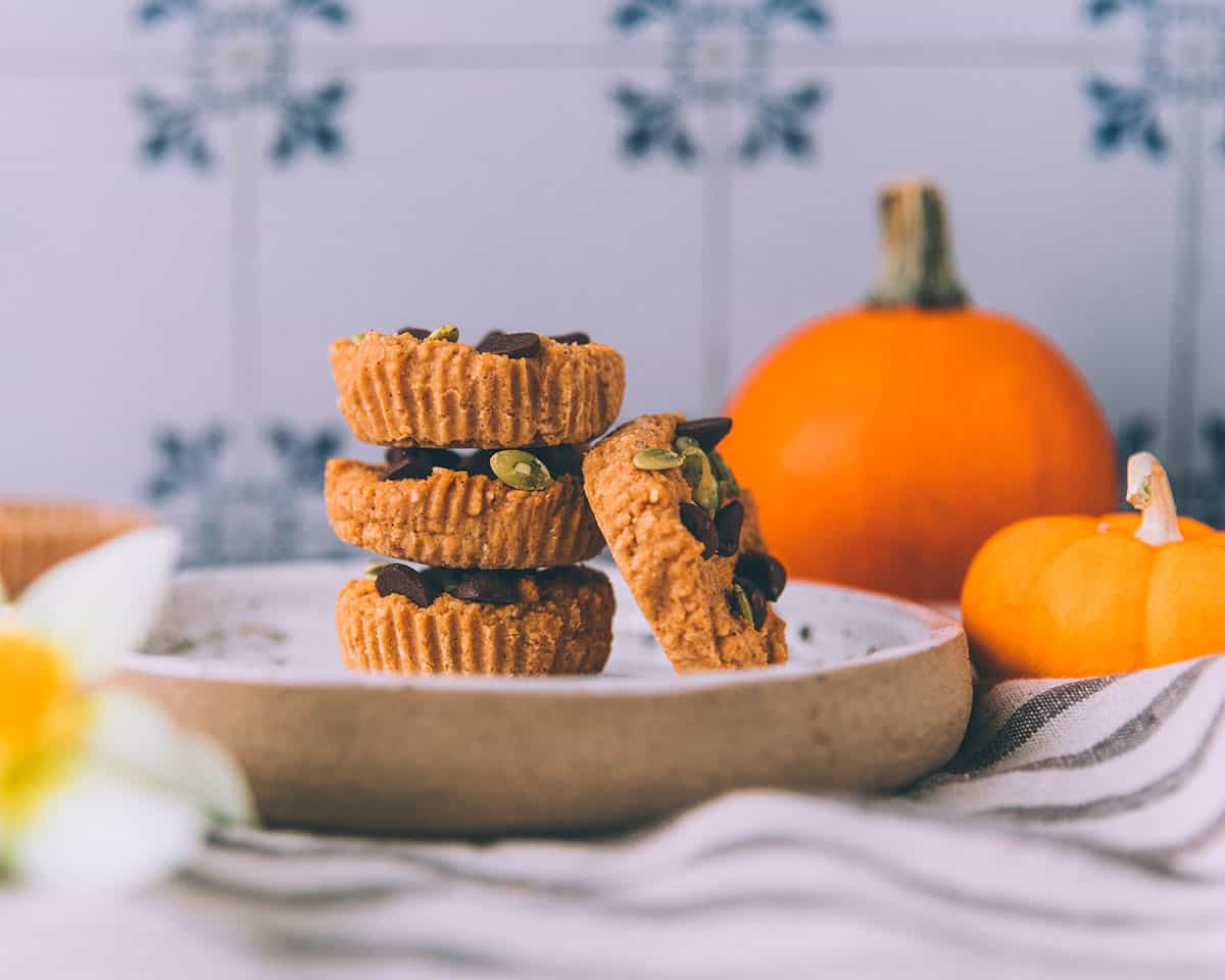 A stack of pumpkin coconut butter cups on a white plate with a pumpkin in the background, side view. 