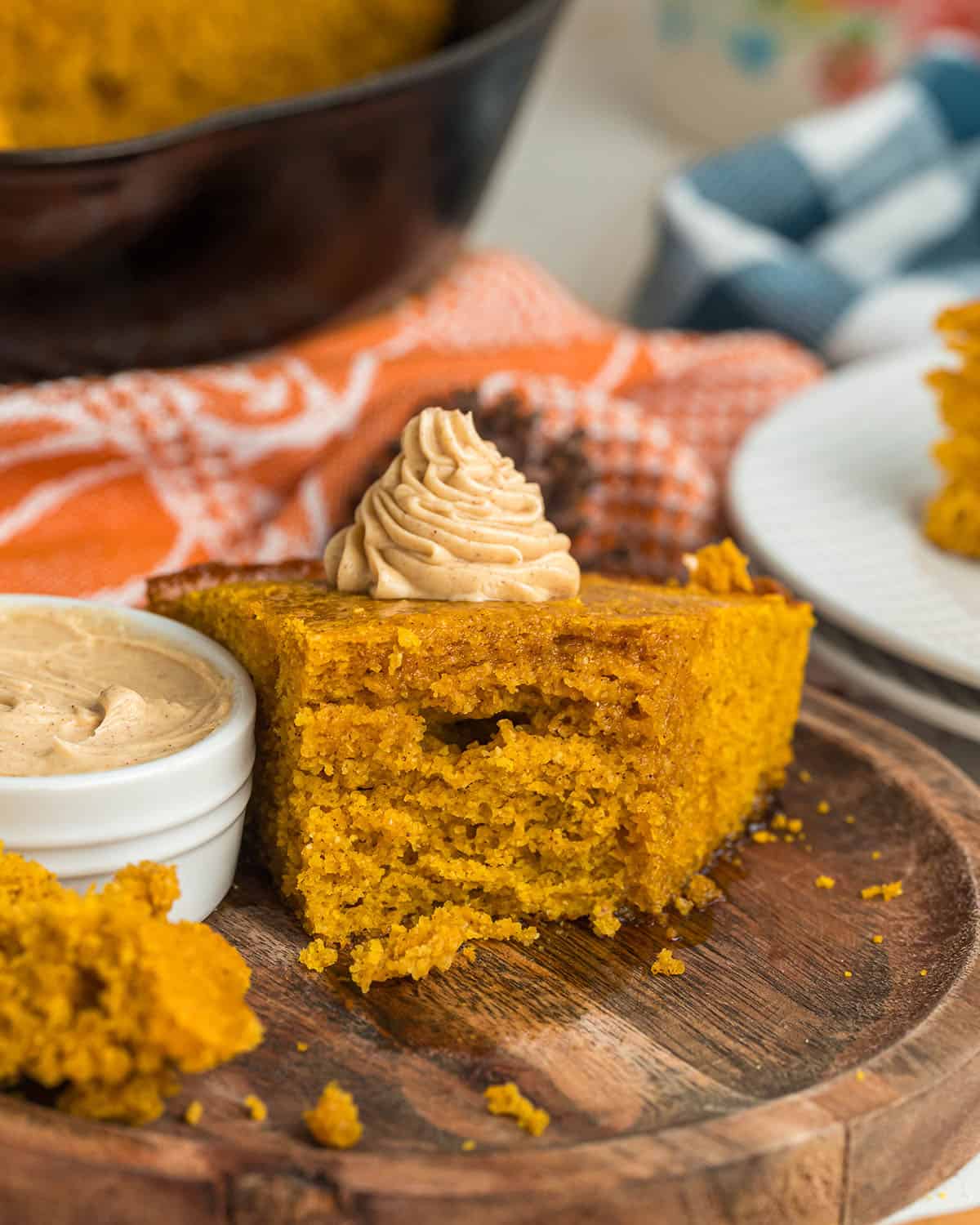 A slice of pumpkin cornbread on a wood plate with a bite taken out of it, topped with piped maple butter. 