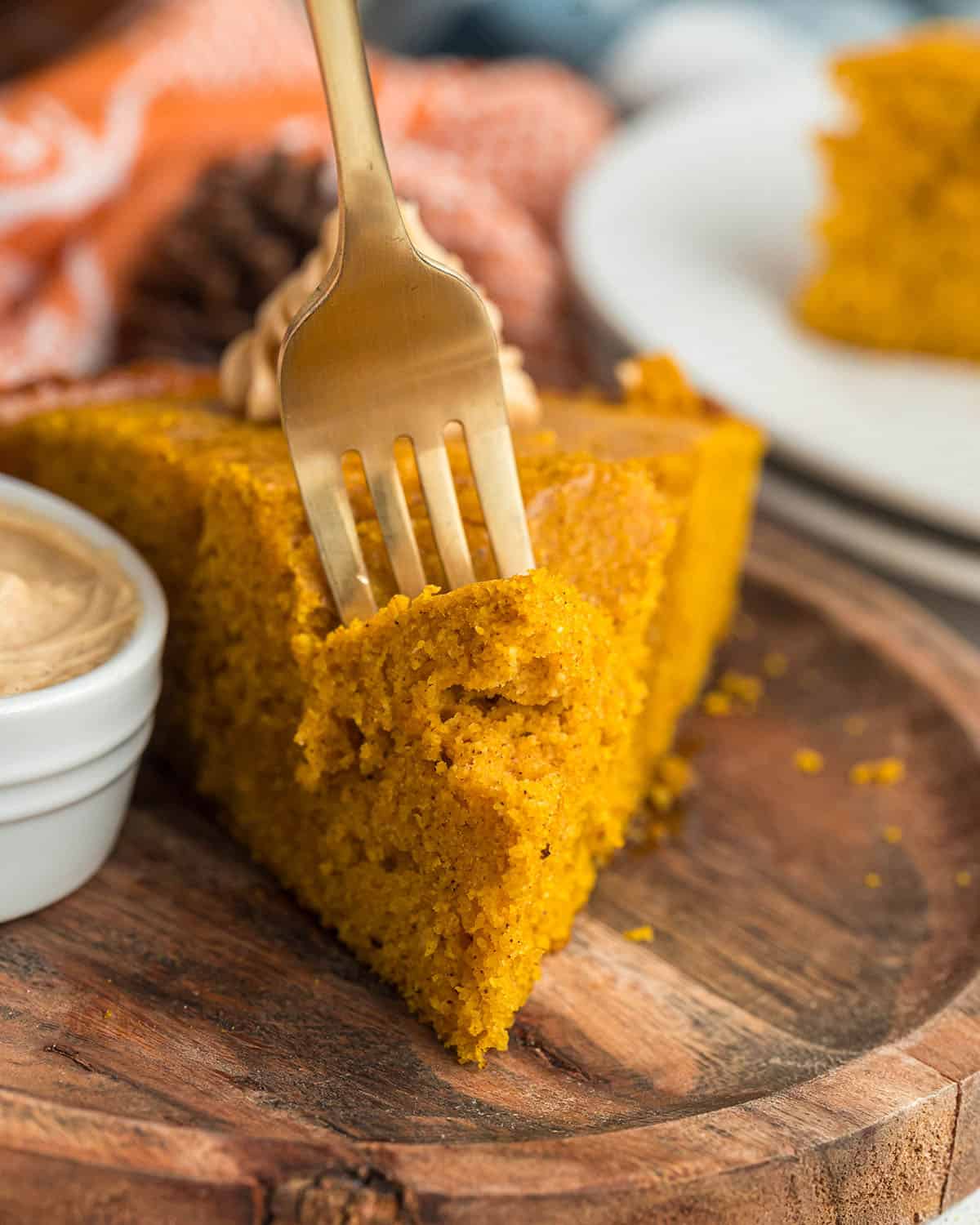A piece of pumpkin bread on a wooden plate with a fork sticking into it. Front view. 