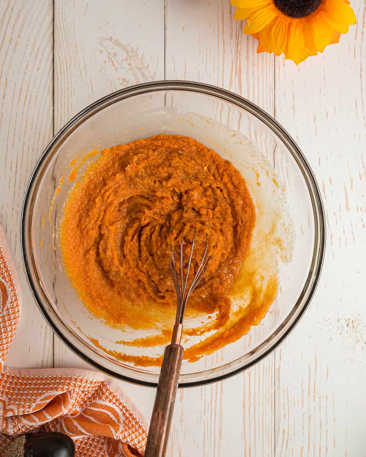 Wet ingredients for pumpkin cornbread being whisked together in a clear bowl, top view.  
