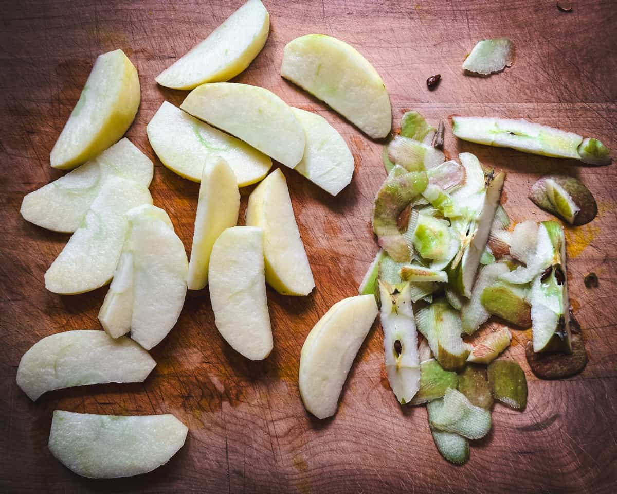 Sliced apples with peels to the side, on a wood cutting board. 