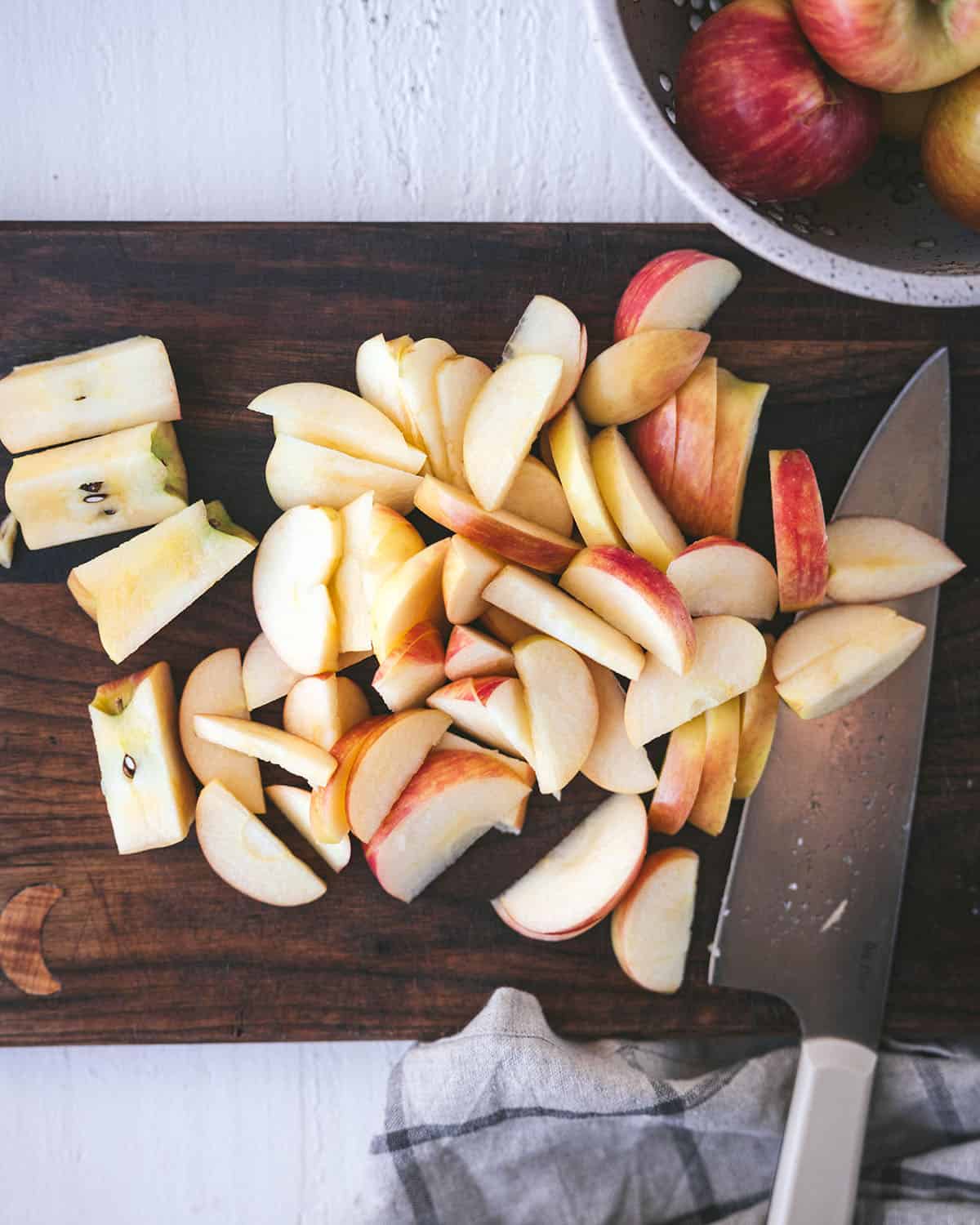 A dark wood cutting board with sliced apples on it and a large knife next to the slices. 