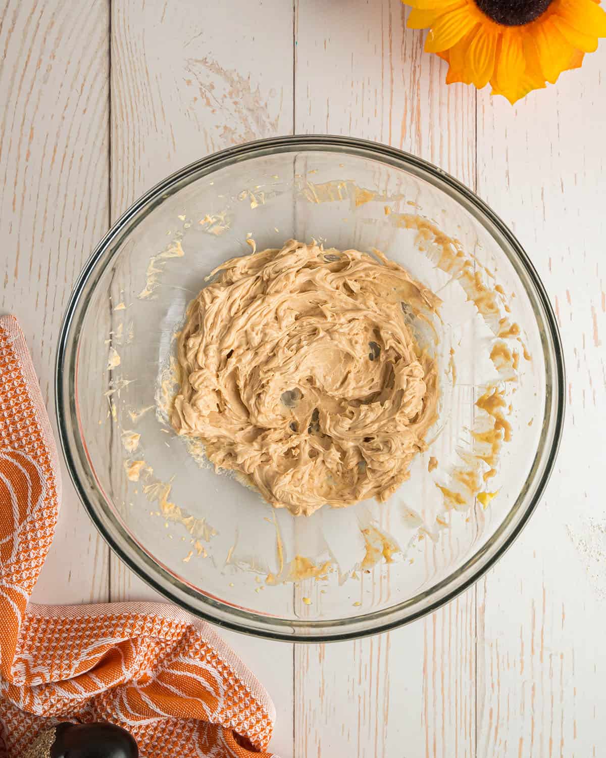 Whipped maple butter in a clear bowl, on a white wood surface surrounded with and orange and white towel. 