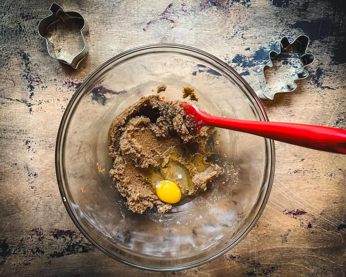 An egg and vanilla being stirred into the butter an sugar with a red spatula, top view. 