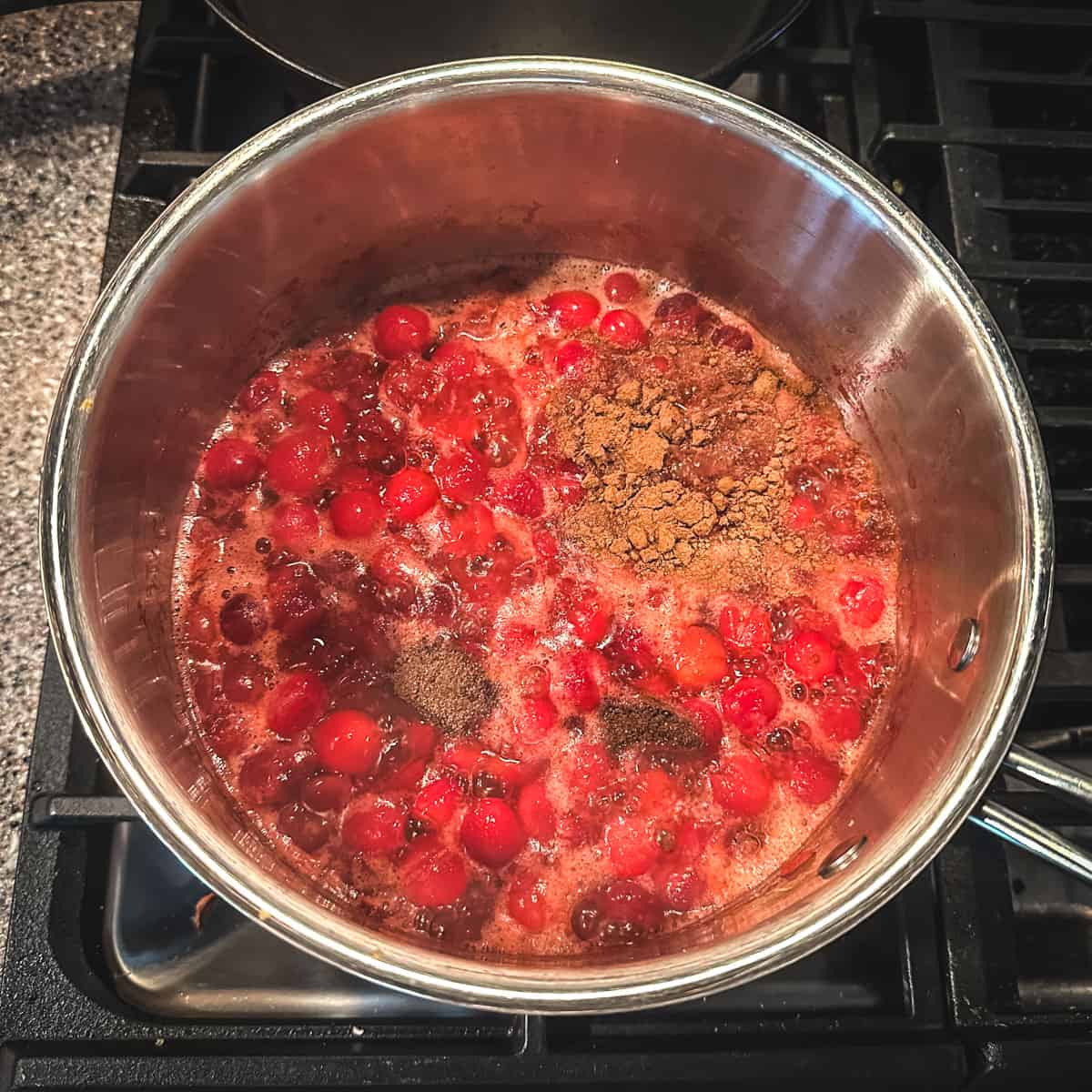 Spices being added to a pot with boiled cranberries, top view. 