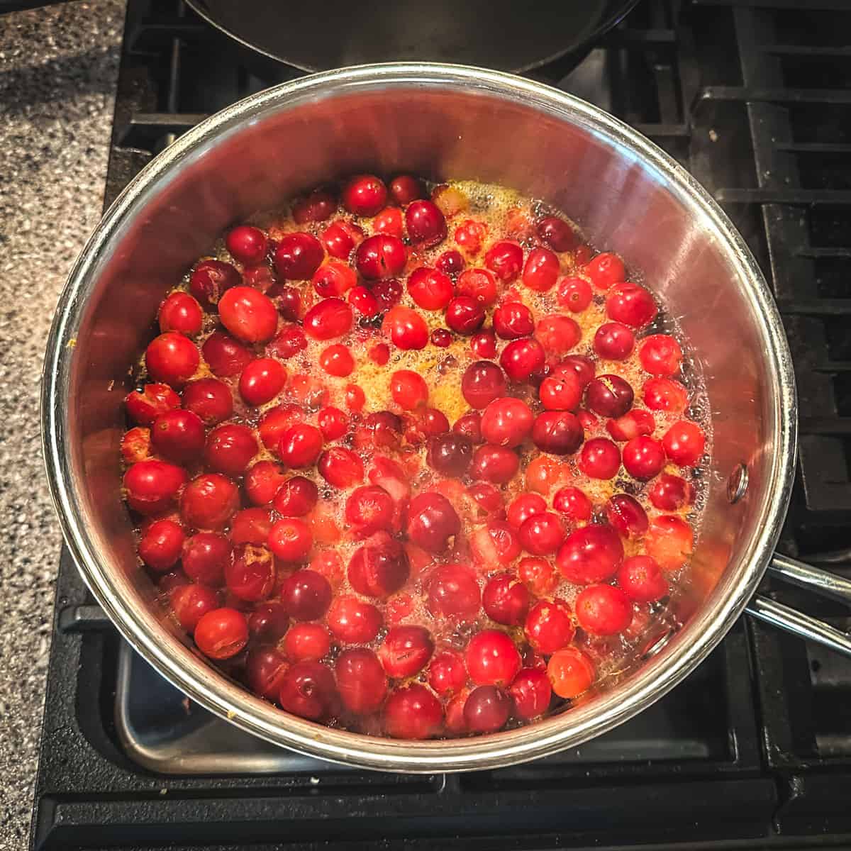 Cranberries and other ingredients boiling in a pot, top view. 