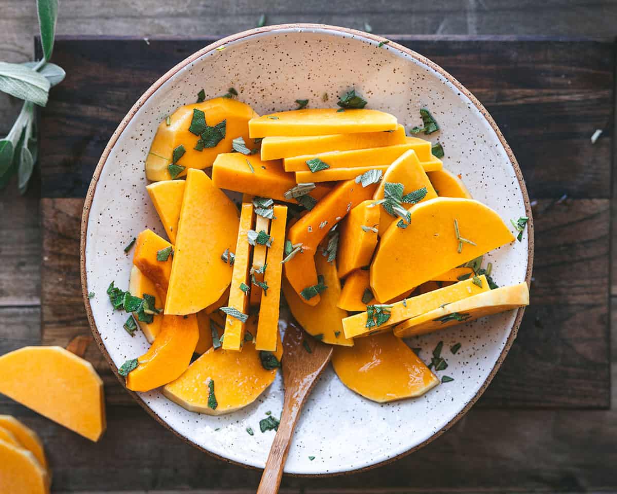 A bowl with squash slices being mixed with a wooden spoon, top view. 