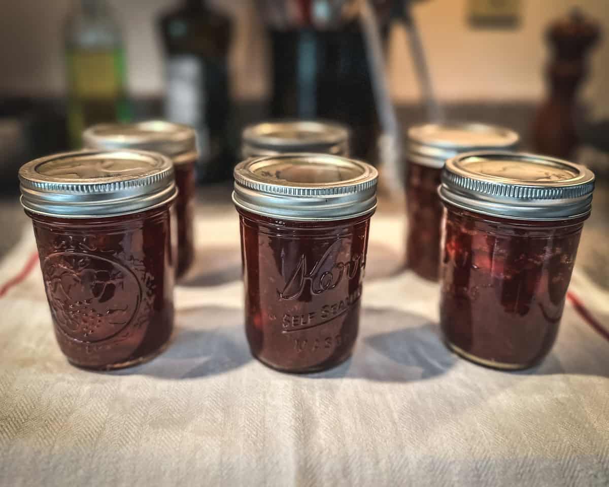 Jars of canned cranberry sauce cooling on a towel on the counter. 