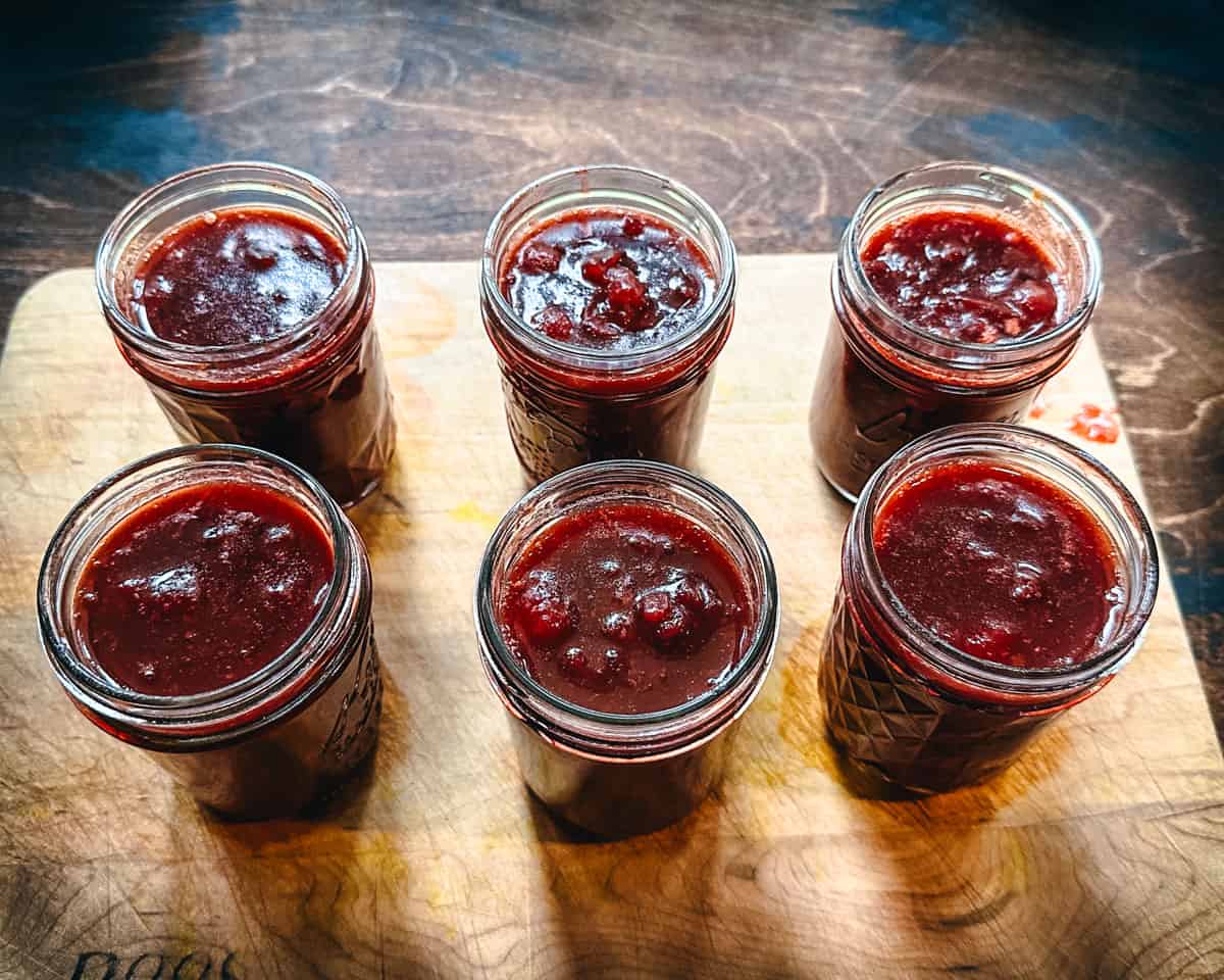 6 jars of cranberry sauce without lids sitting on a wood cutting board. 