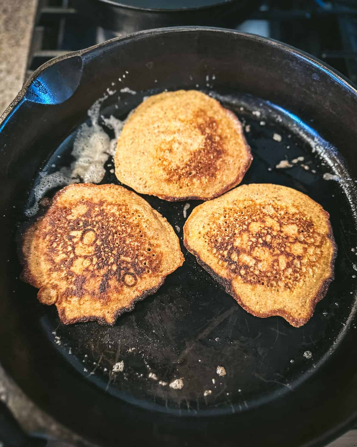 Acorn pancakes browned on one side and cooking on the other in a cast iron pan. 